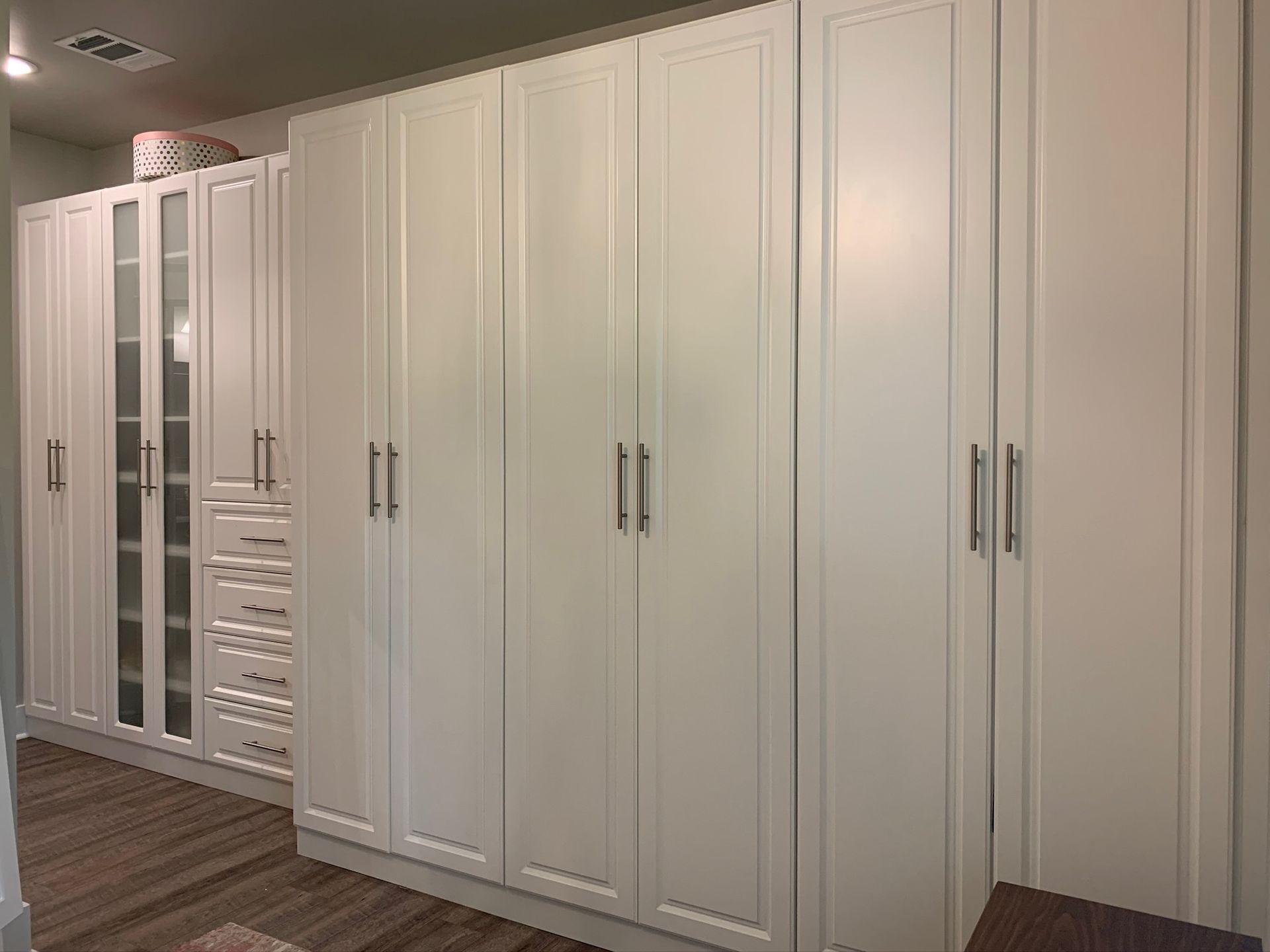 White closet cabinets with tall doors and silver handles in a well-lit room.