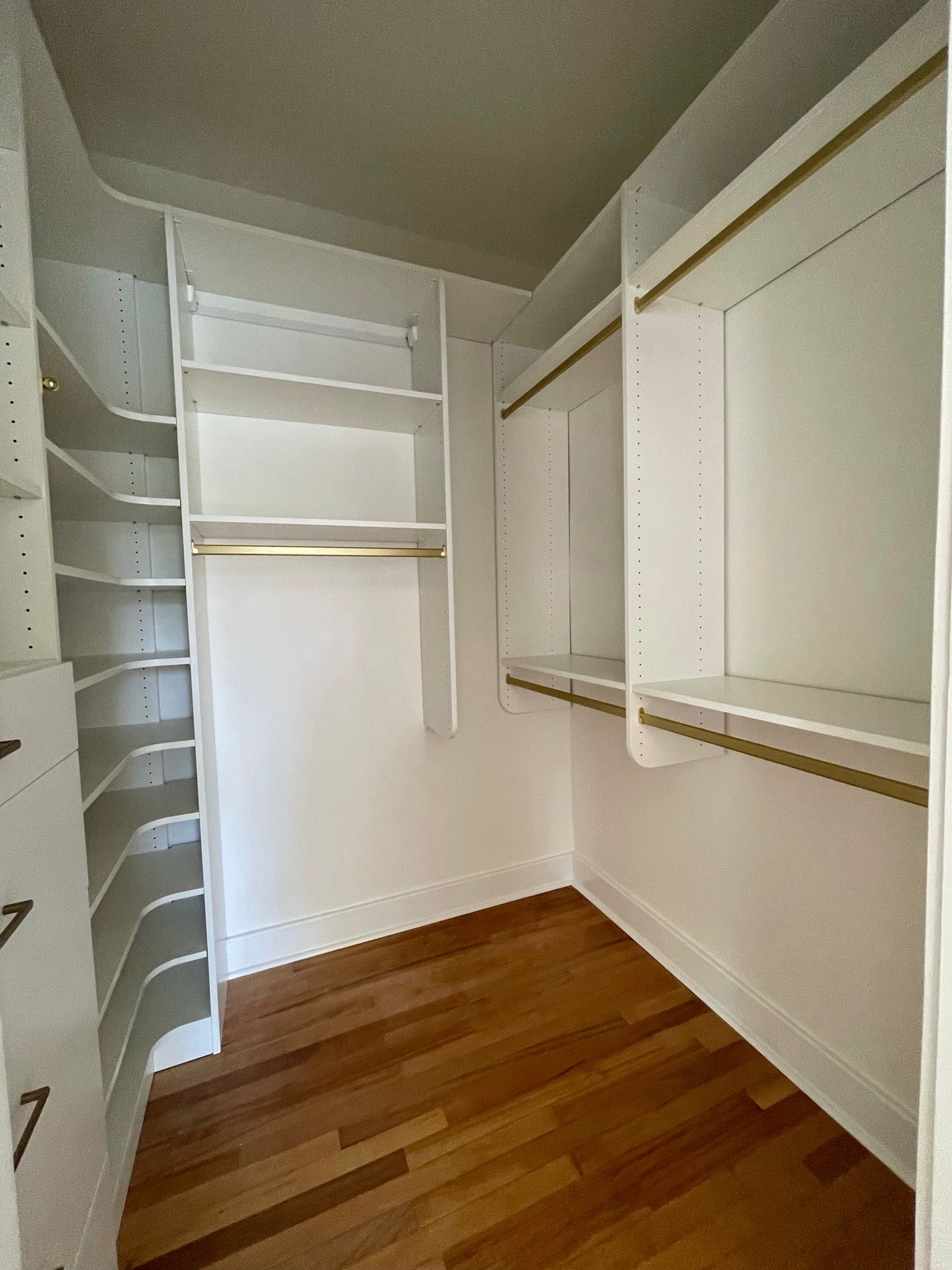 Empty white closet with built-in shelves and a wooden floor.
