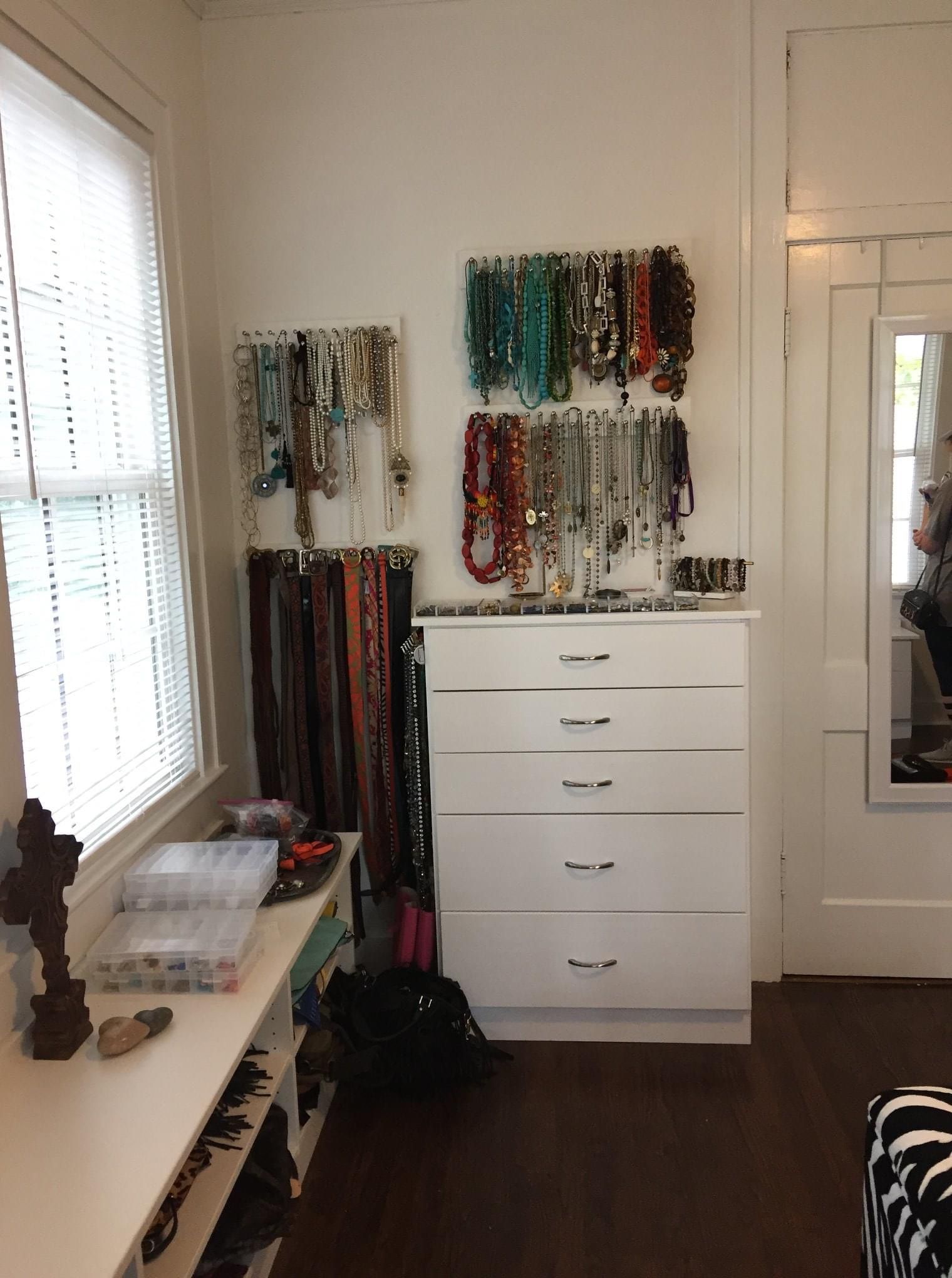 White dresser with jewelry display, belts, window, and mirror.