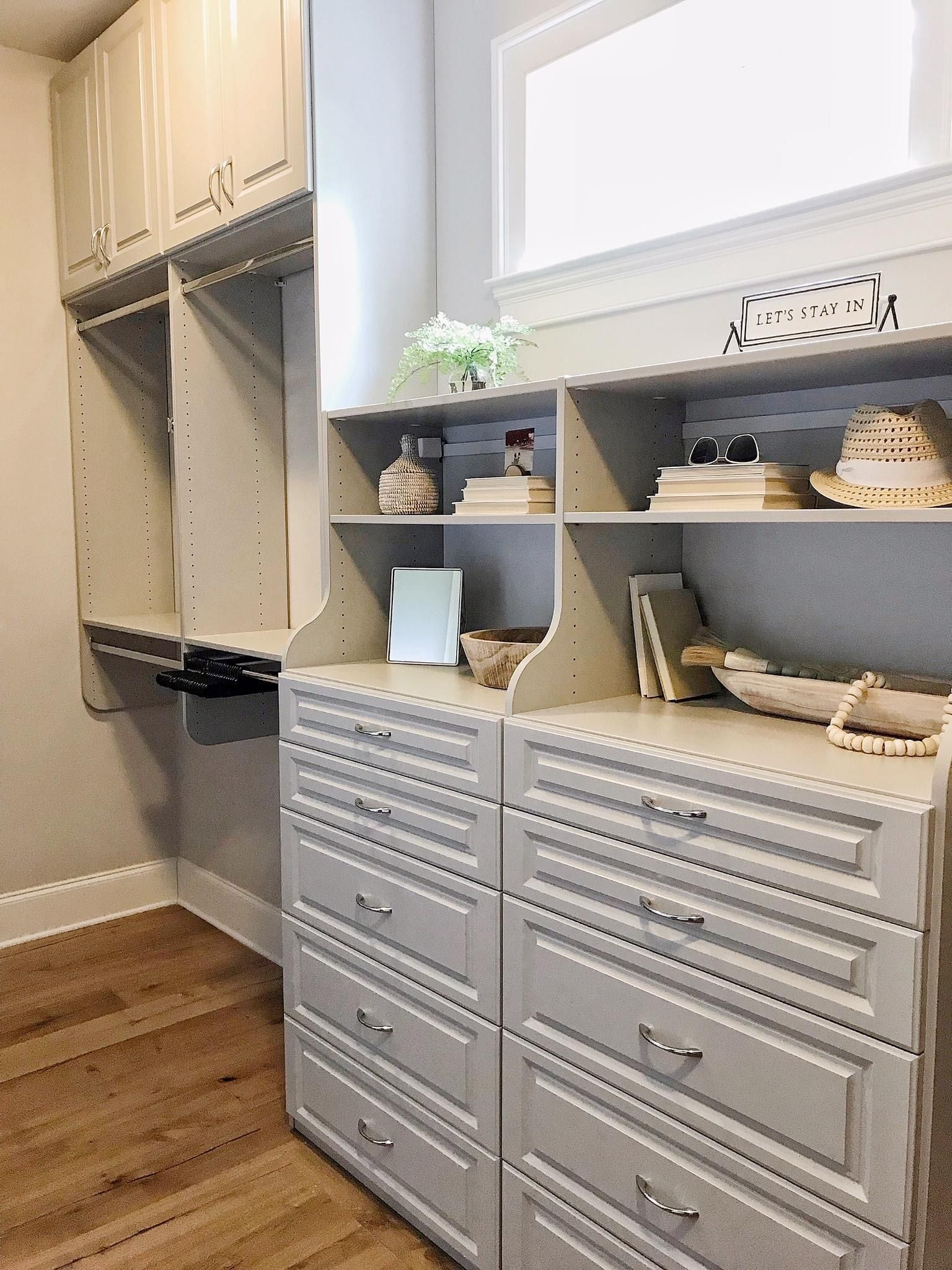 Light gray custom closet with shelves, drawers, and hanging rods. Includes decorative items.