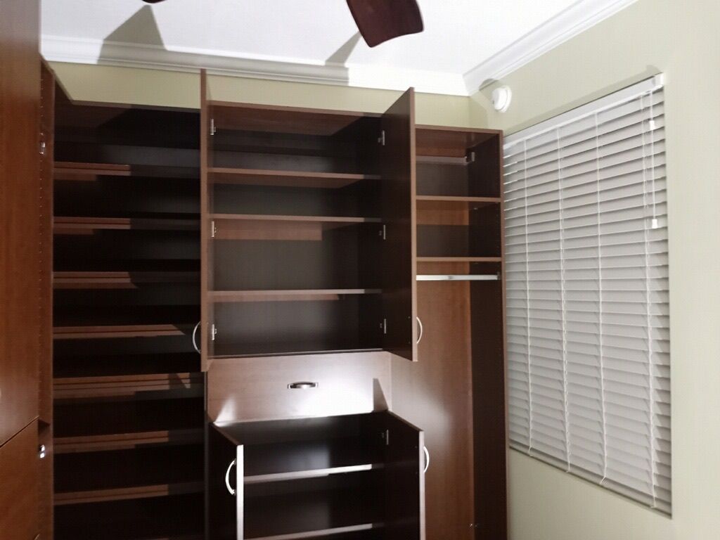 Brown open closet with shelves and a hanging rod, next to a window with white blinds.