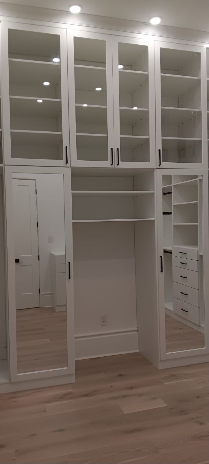 White custom closet with glass-fronted upper cabinets, mirrored doors, and shelving.