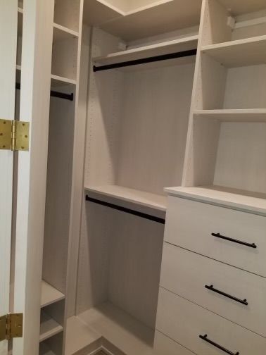 White closet with shelves, drawers, and hanging rods. Black hardware and door hinges.