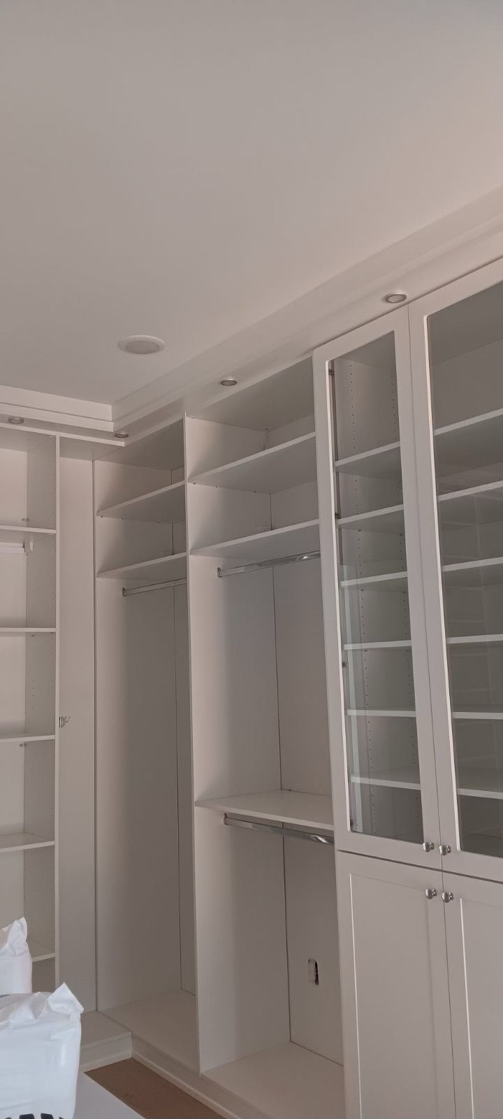 White custom closet with shelves, hanging rods, and glass-paneled doors.