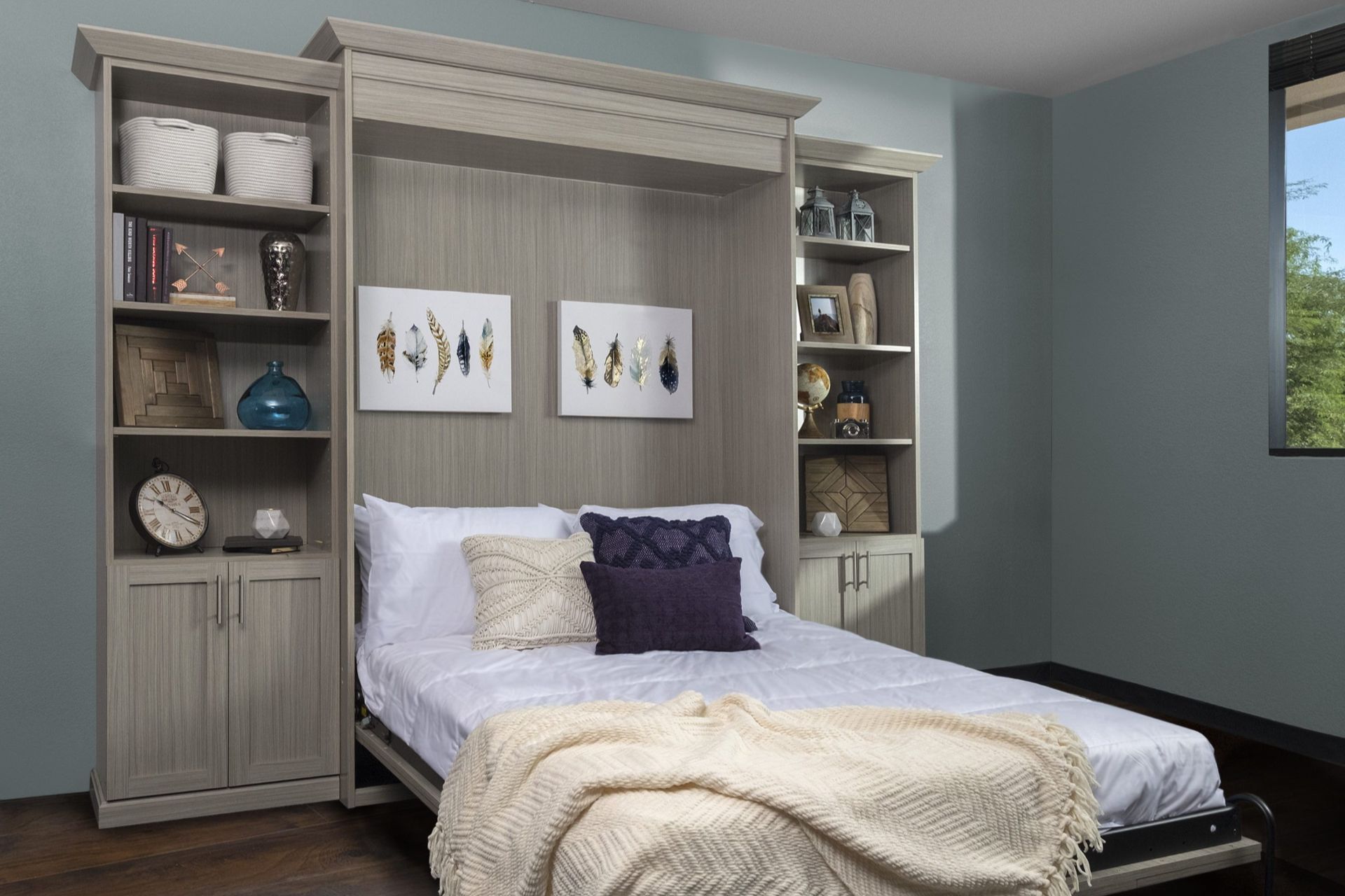 A Murphy bed integrated into a wooden cabinet with bookshelves on either side. The bed is made, with throw pillows and a blanket.