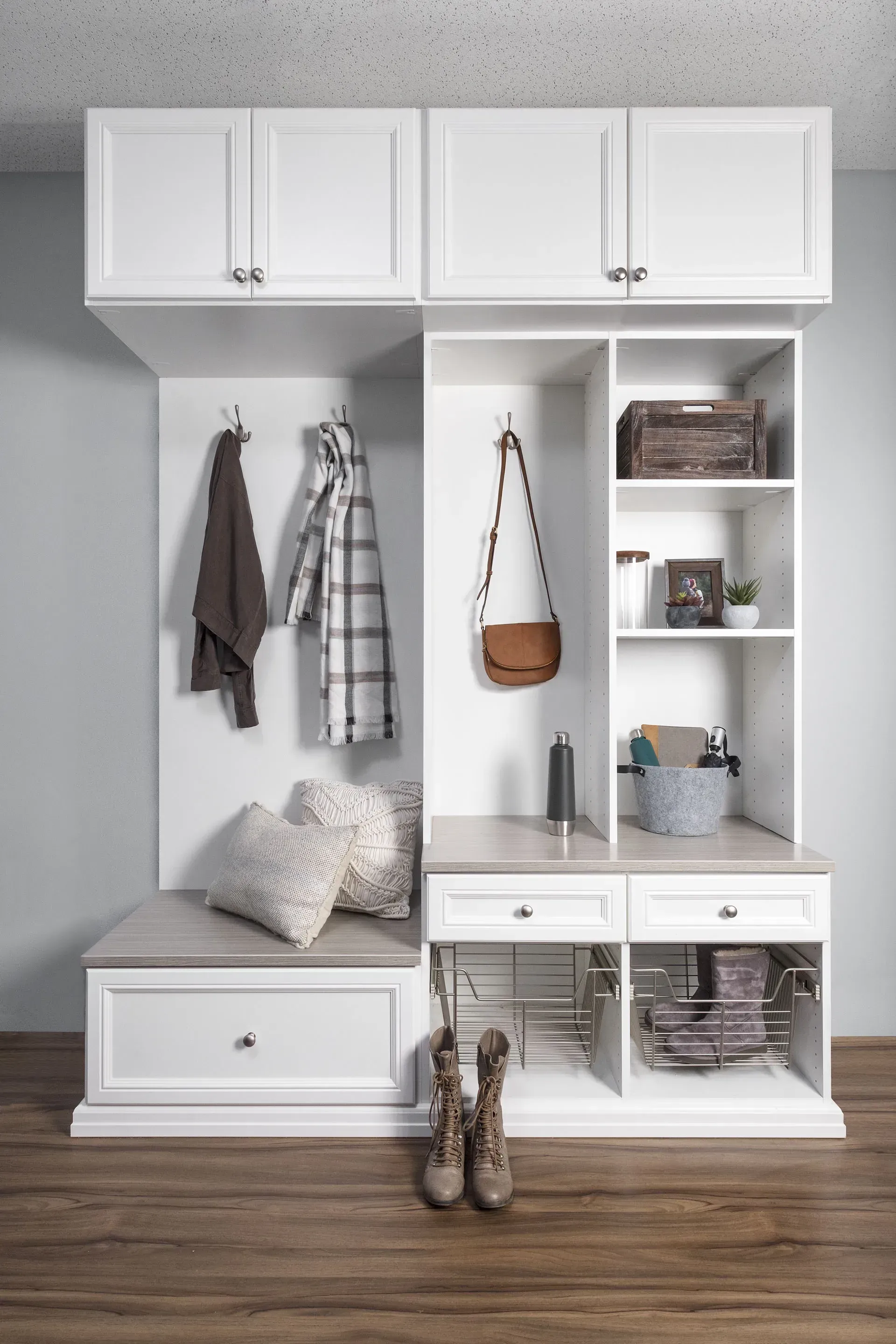 White built-in entryway organizer with bench, hooks, and storage cabinets on a wood floor.