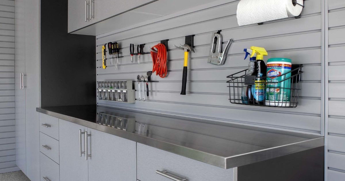 Garage workbench with gray cabinets, metal countertop, and tools hanging on a slatted wall.