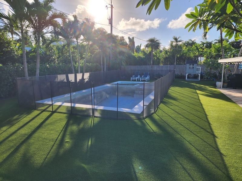 A fence surrounds a large swimming pool in a backyard.