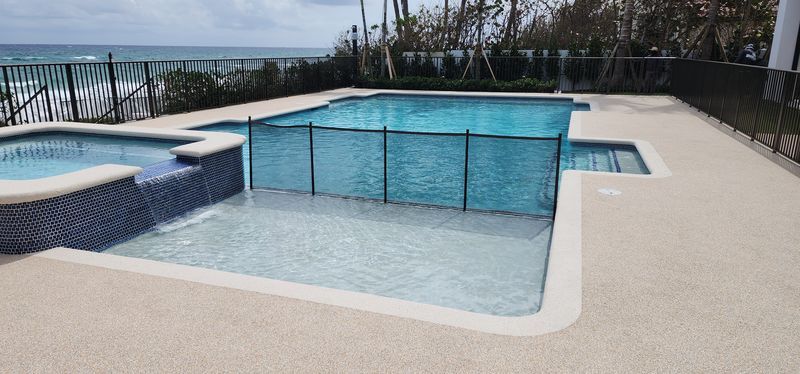 A large swimming pool with a fence around it and a hot tub next to it.