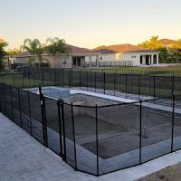 A fence around a swimming pool with a gate and a house in the background.