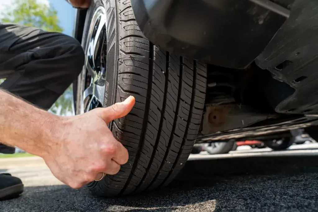 Person checking a car tire's tread with their hand, outdoors.