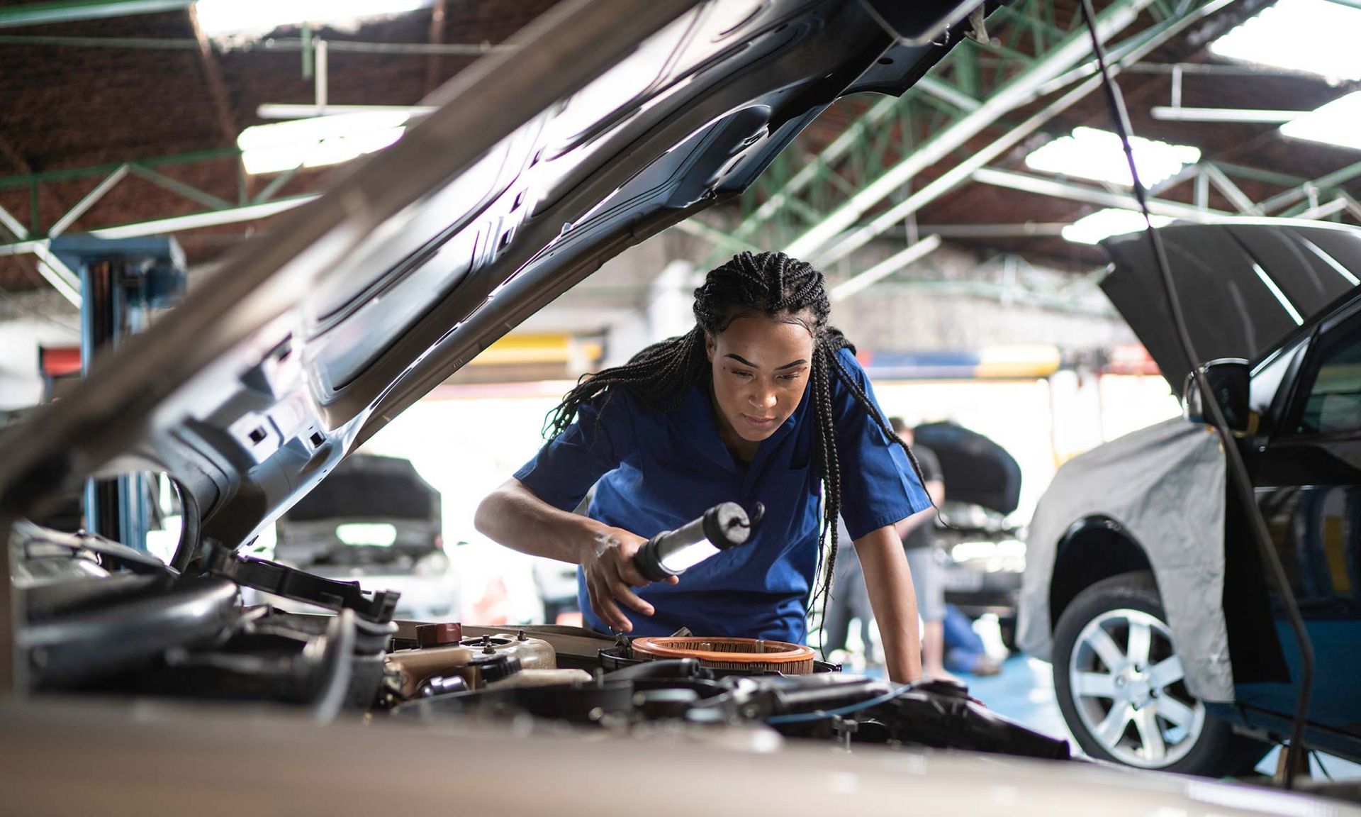 Mechanic examines engine with flashlight in auto shop.