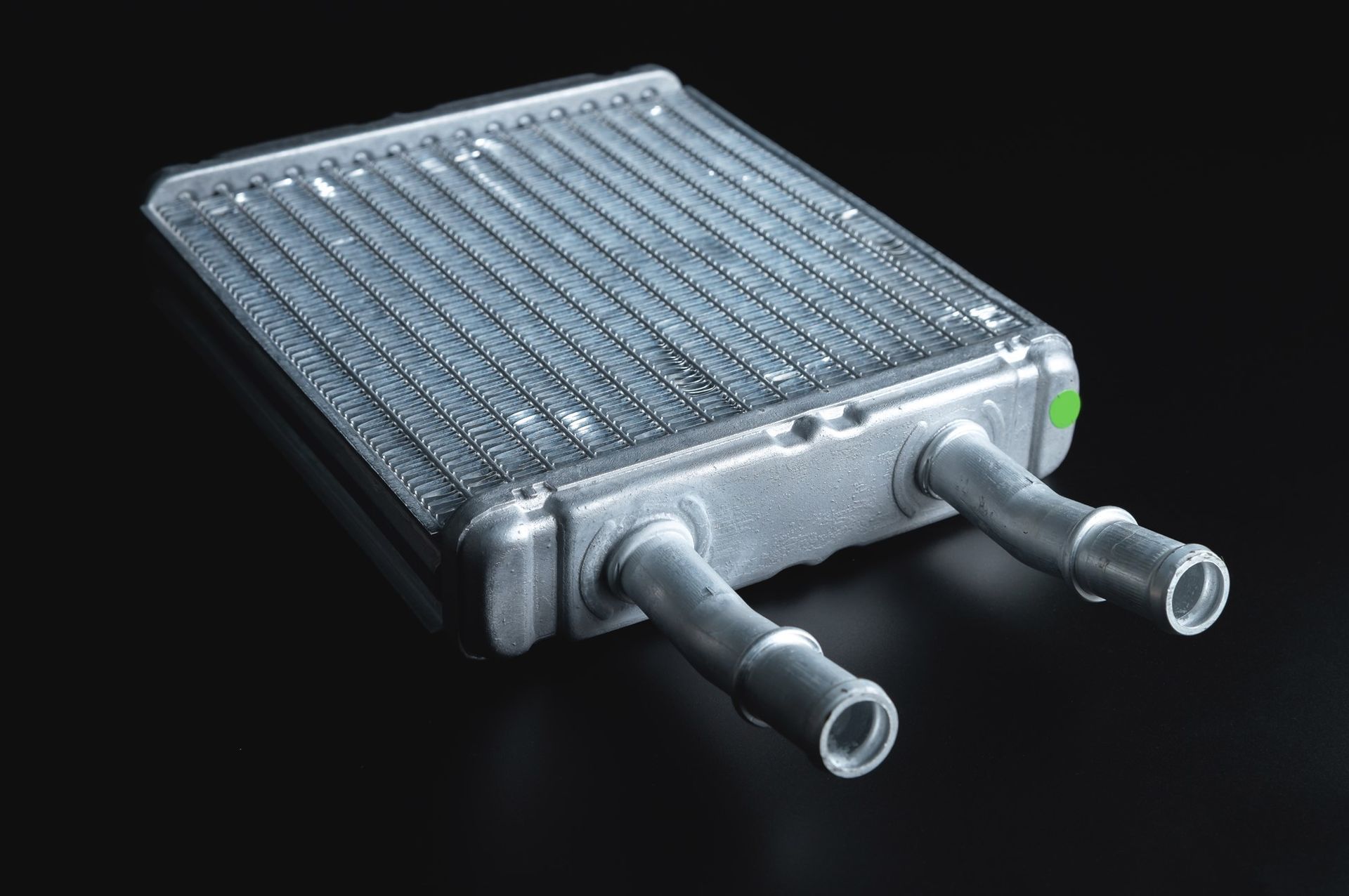 Car heater core, silver with two attached tubes, on black background.
