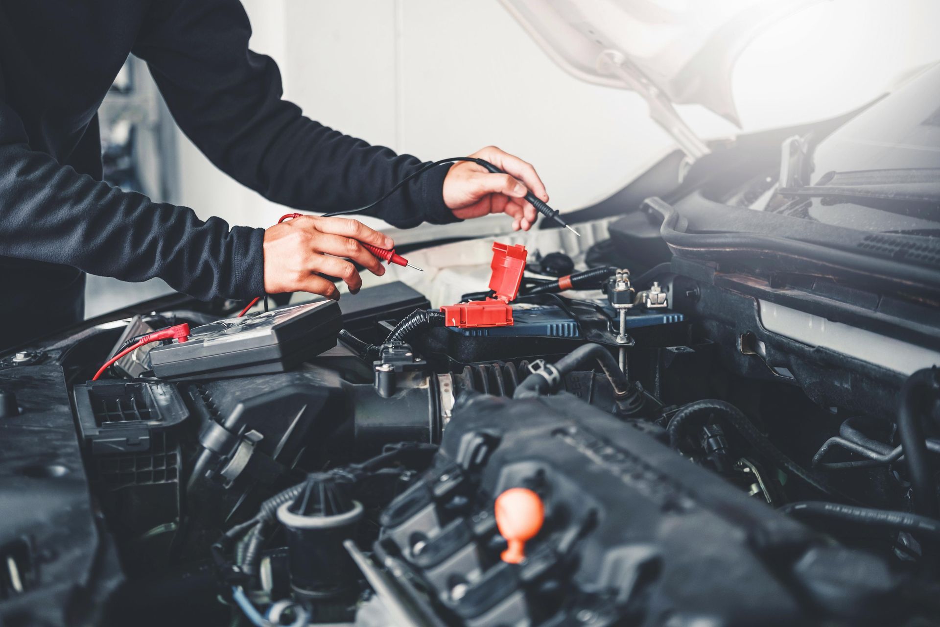 Mechanic working on car engine, using tools under the hood. Bright lighting.
