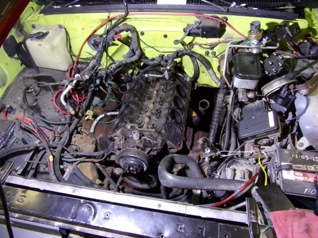 Yellow vehicle engine bay with engine, wiring, and components visible.