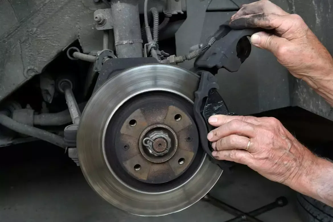 Hands holding a brake pad near a car's brake disc.