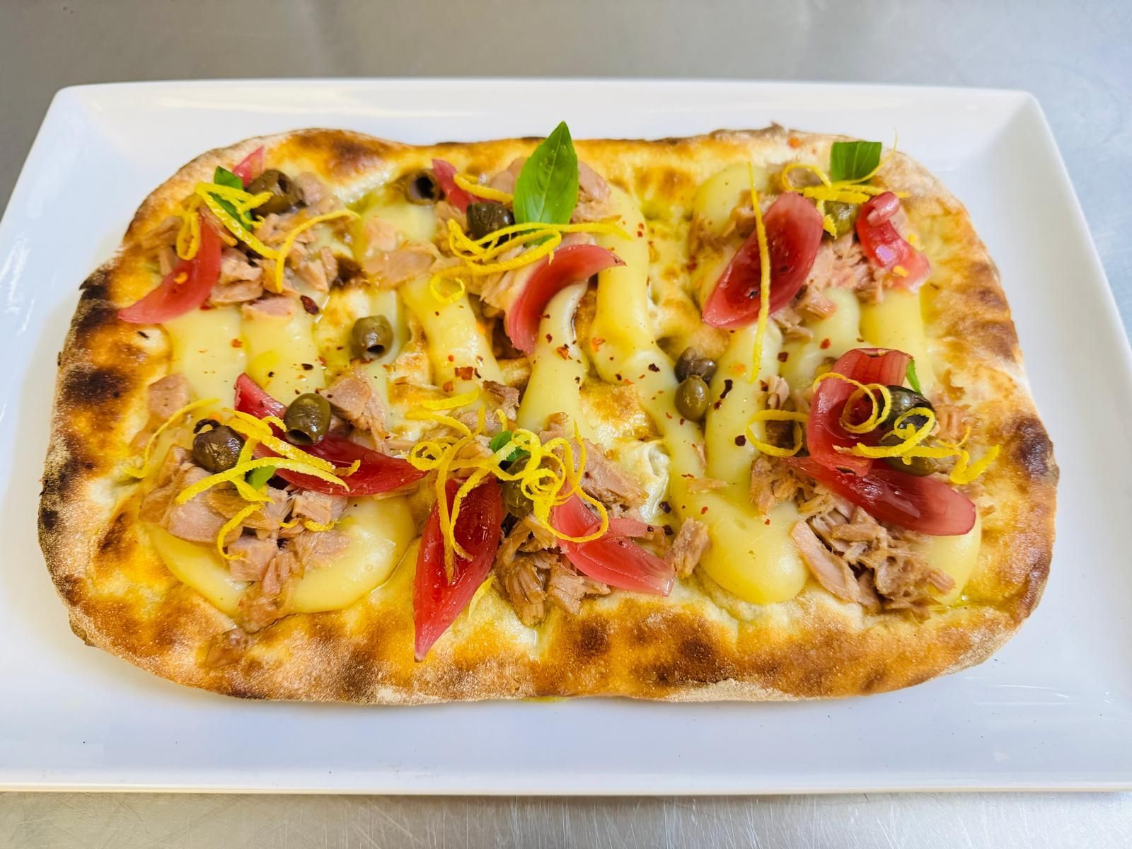 Una pizza con tanti condimenti è servita su un piatto bianco.