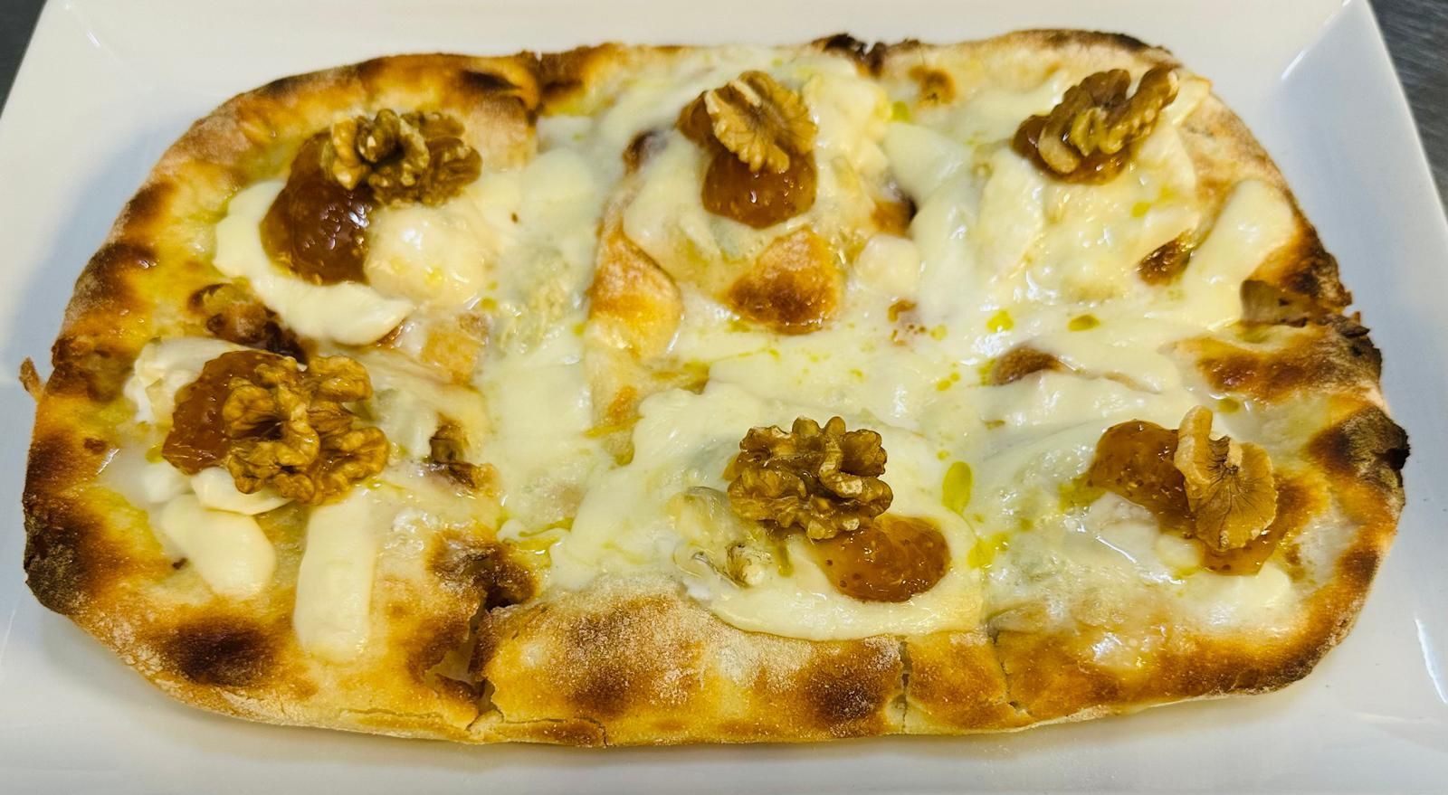 Una pizza con formaggio e noci su un piatto bianco.