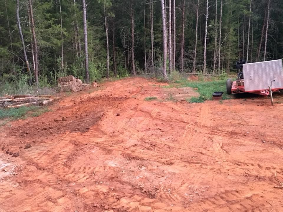 A trailer is parked in a dirt field in the middle of a forest.