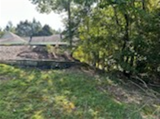 A house is sitting in the middle of a grassy field surrounded by trees.