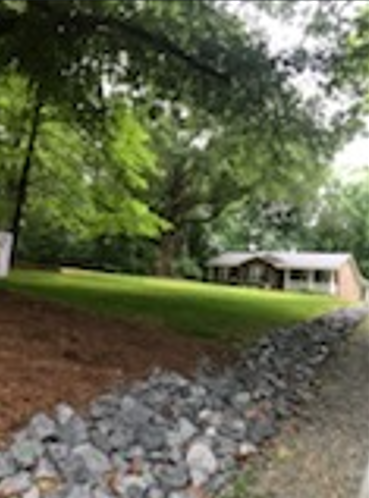 A house is sitting in the middle of a lush green field surrounded by trees.