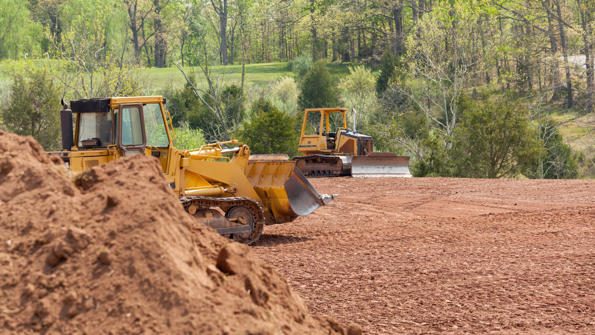 Two bulldozers are working on a dirt field.