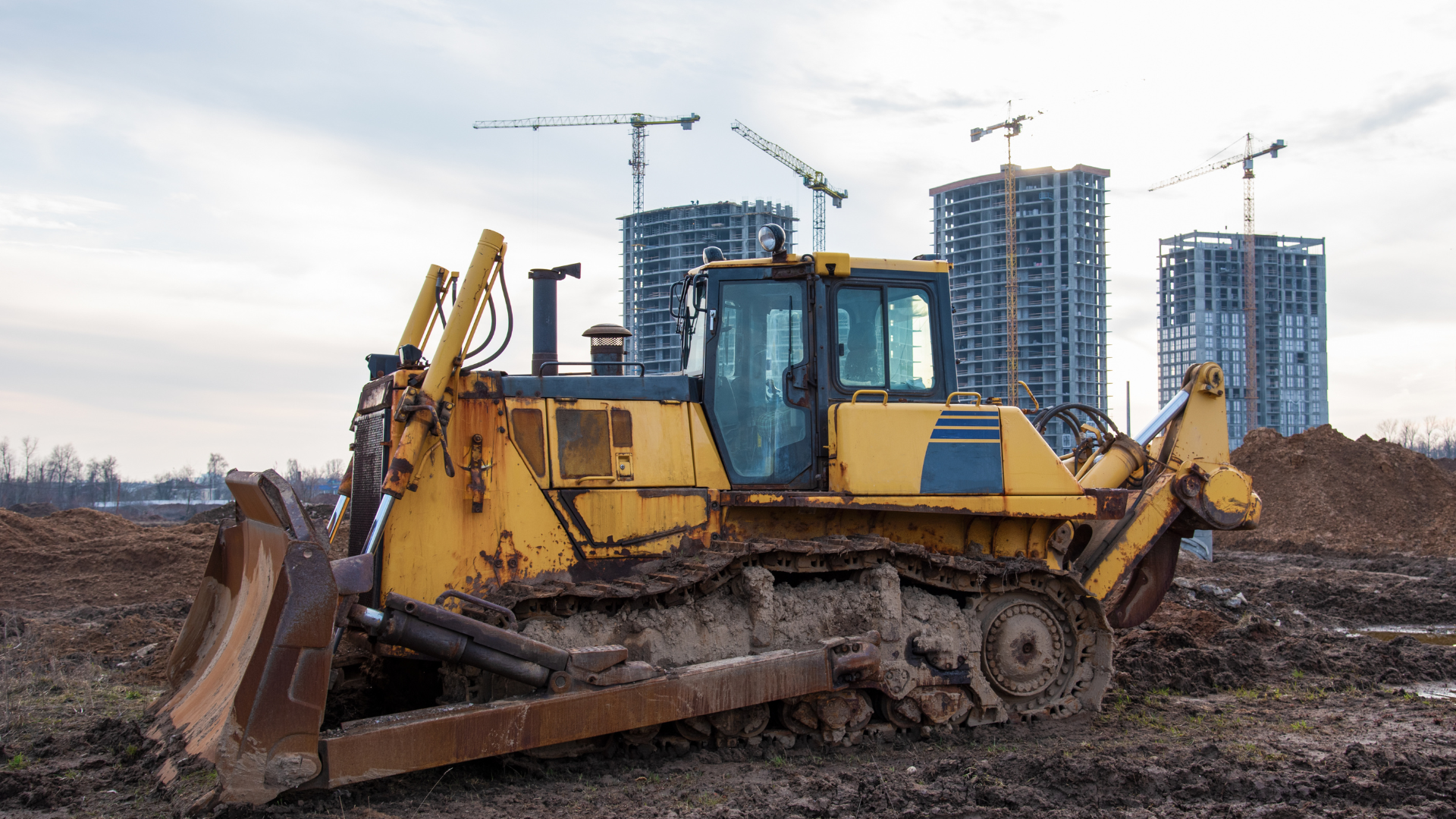 A yellow excavator is sitting in the middle of a dirt field.