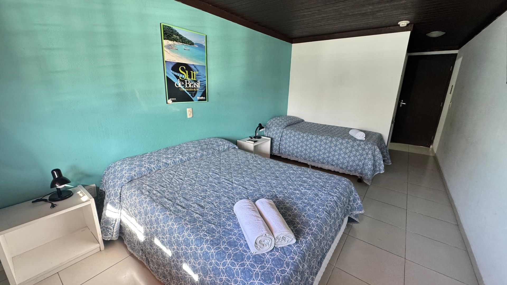 Duas camas em um quarto com paredes azul-petróleo, uma obra de arte, mesas de cabeceira brancas e um teto marrom escuro.