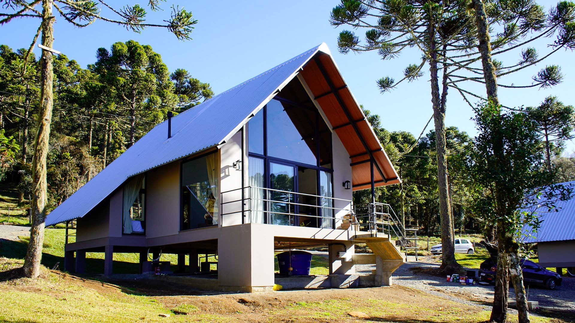 Cabana moderna com janelas grandes, sobre palafitas, em uma área florestal.