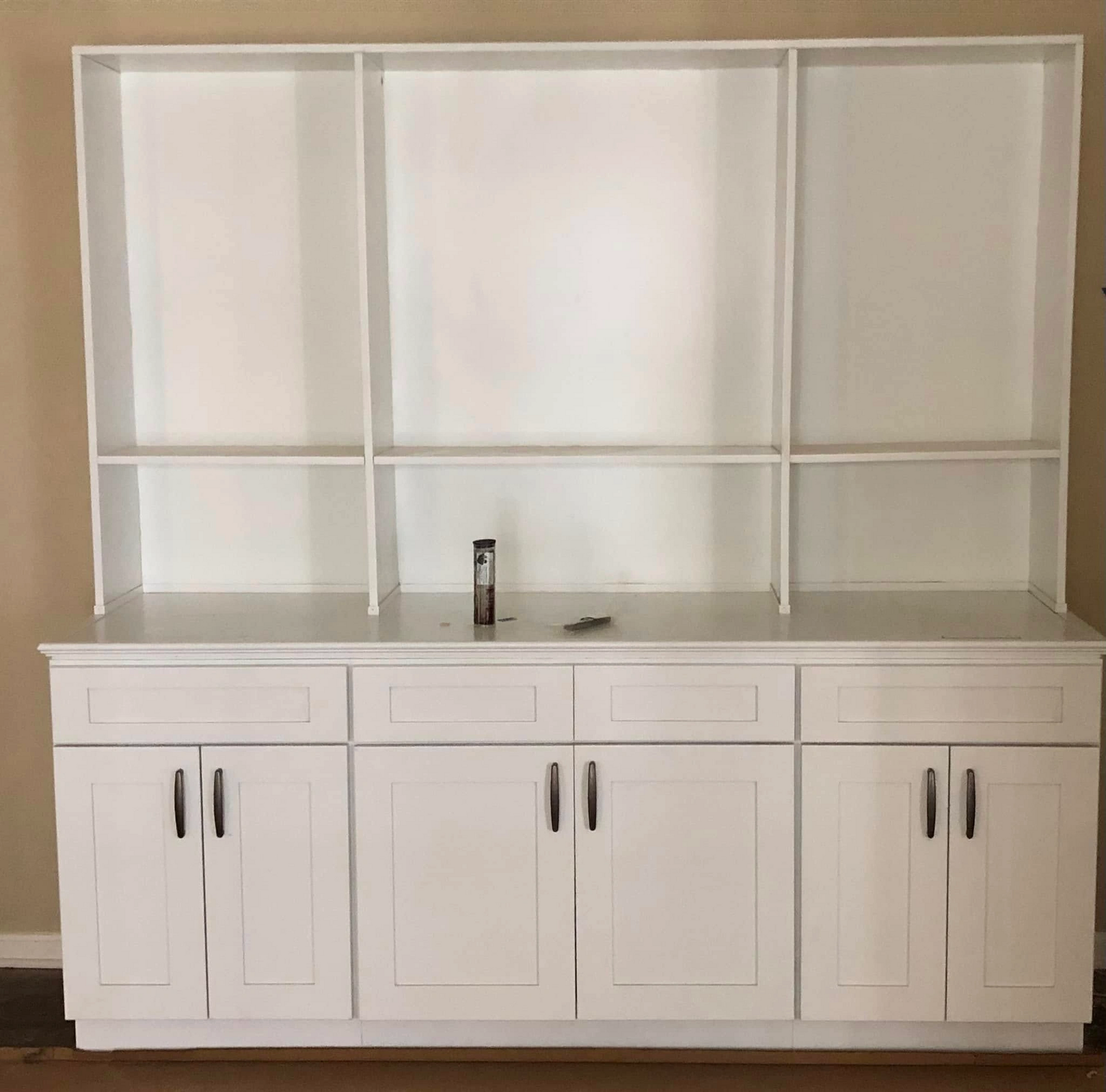 White built-in cabinet with upper shelves and lower cabinet doors and drawers, against a tan wall.
