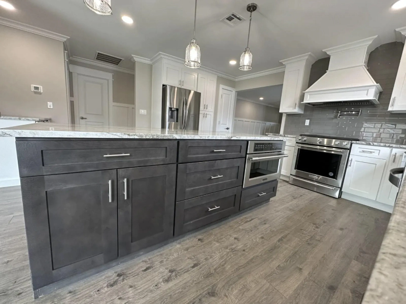 Modern kitchen with a large gray island, stainless steel appliances, and white cabinets. Wooden floor.
