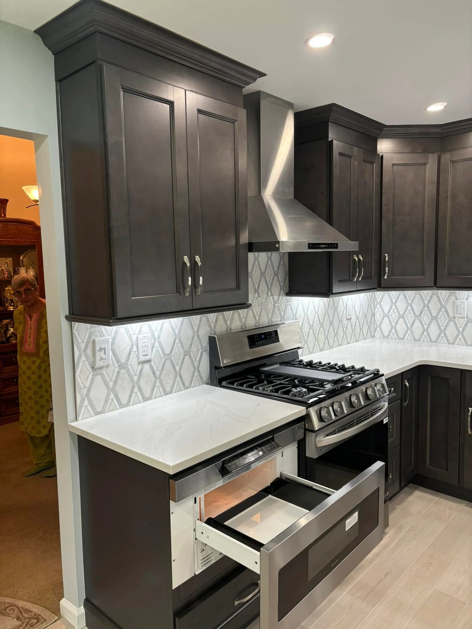 A modern kitchen with dark cabinets and a stainless steel range. A microwave drawer is open, with a light-colored countertop.