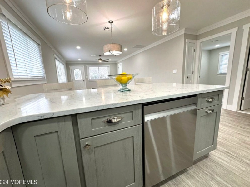 A modern kitchen with gray cabinets, a stainless steel dishwasher, and a white countertop. There are pendant lights and a bowl of lemons.