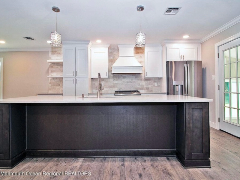 Modern kitchen with dark island, white cabinets, and stainless steel appliances. Light-colored flooring and a glass-paneled door.