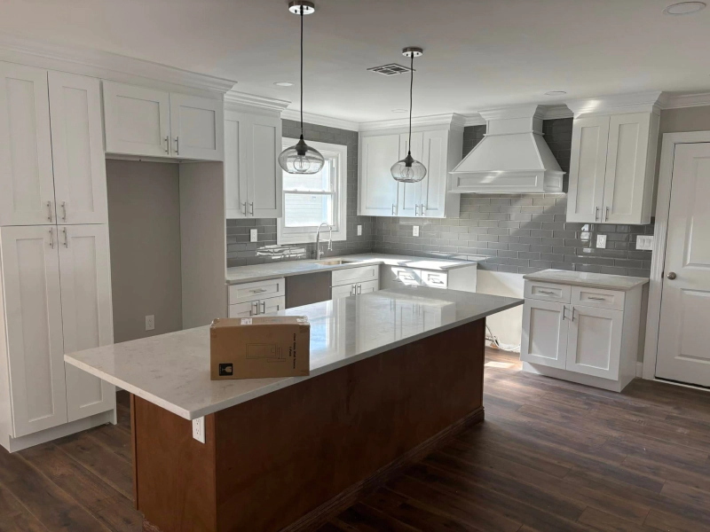 White kitchen with a dark brown island. Features include white cabinets, grey backsplash, and wood-look flooring.