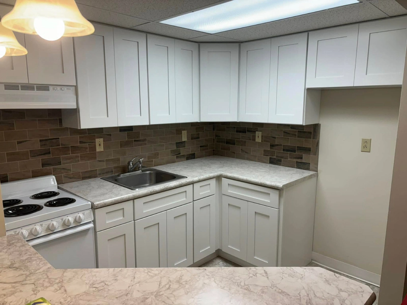 A small, white kitchen with light-colored countertops, a brick-look backsplash, and a white stove.