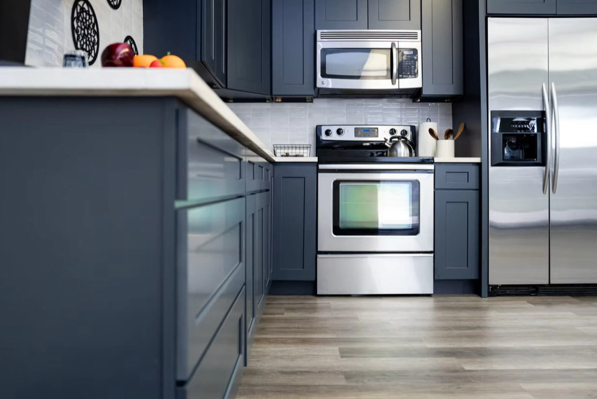 Modern kitchen with blue cabinets, stainless steel appliances, and light wood-look flooring. White countertops and a small backsplash.