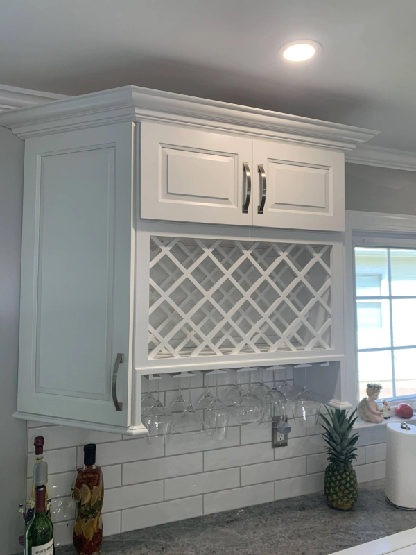 White kitchen cabinets with a wine rack, wine glasses hanging below, and a pineapple on the countertop.