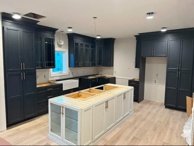 A newly remodeled kitchen with black cabinets, a white island, and light wood flooring.