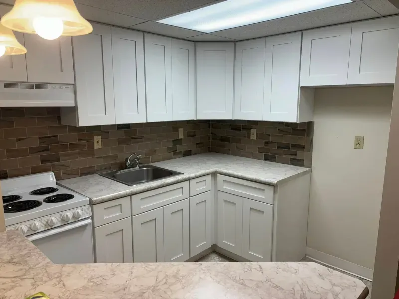 White kitchen with white cabinets, a stove, a sink, a light-colored countertop, and a brown backsplash.