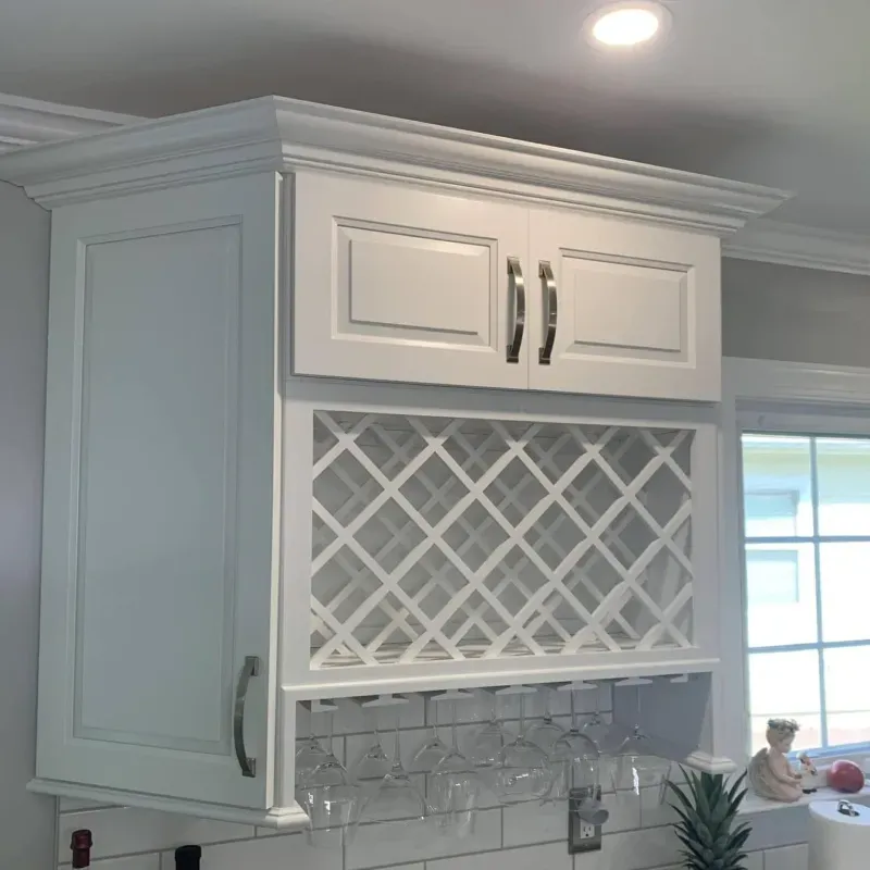 White kitchen cabinet with built-in wine rack and glass holder. Cabinet is mounted above a tiled backsplash near a window.