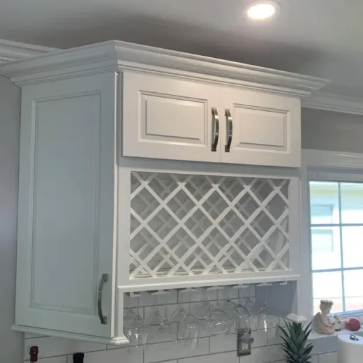 White kitchen cabinet with built-in wine rack and glass holder. Cabinet is mounted above a tiled backsplash near a window.