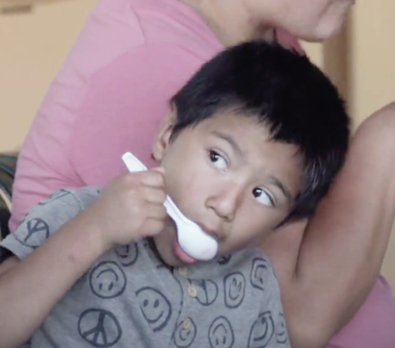 a young boy with a peace sign on his shirt is holding a white spoon in his mouth