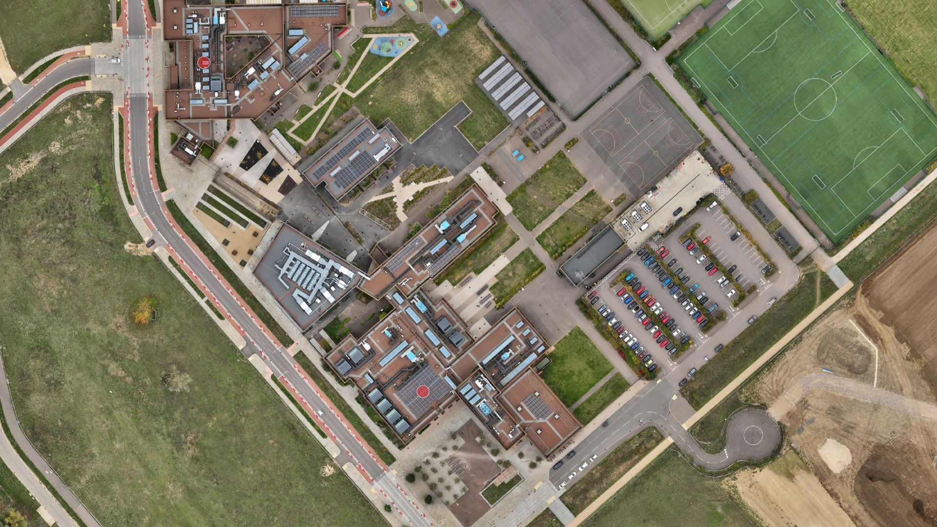 Aerial view of a Northstowe Secondary College complex with buildings, parking areas, sports fields, and surrounding green spaces.