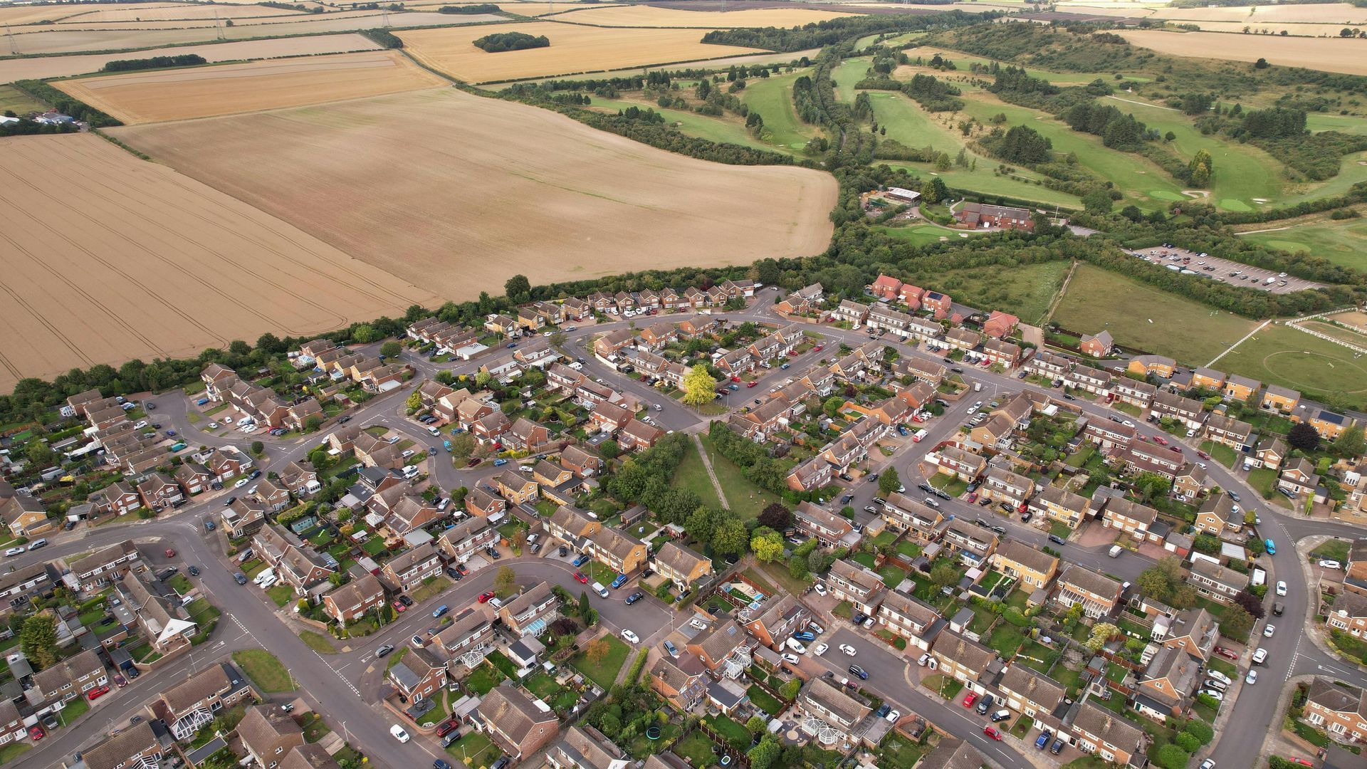 Aerial view of a suburban neighborhood bordering agricultural fields and a golf course.