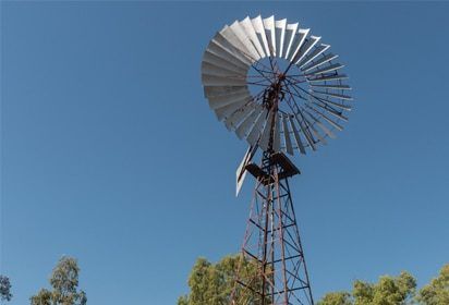 A Large Windmill Against a Blue Sky With Trees in the Background — Peter Maundrell & Company Pty Ltd in Springsure, QLD