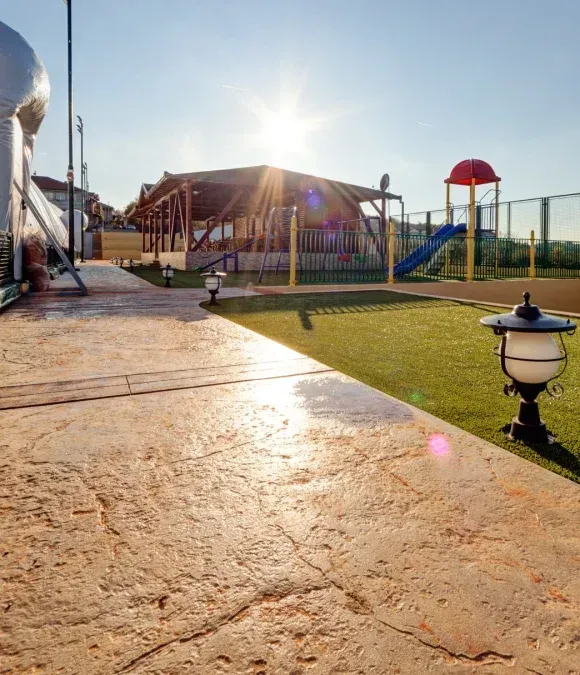 Sunny playground with climbing structure, slide, and lawn beside a paved walkway at sunset