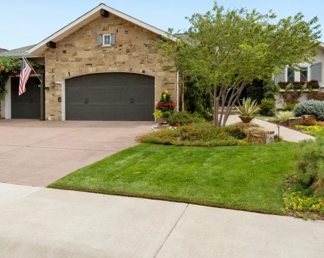 Suburban home with stone facade, dark garage door, and neatly landscaped front yard.