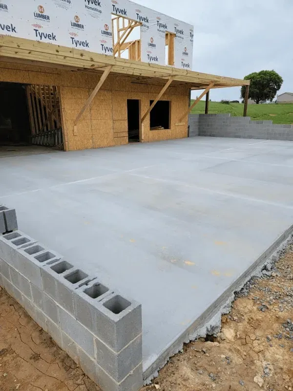 Fresh concrete slab beside a wood-framed building with cinder blocks in the foreground