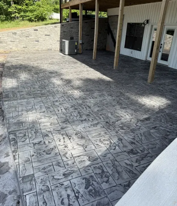 Stamped concrete patio beside a house with porch posts and a small air conditioner unit.
